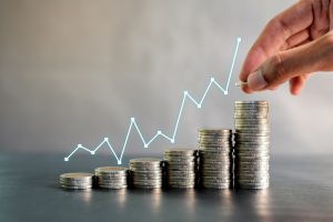 Hand stacking coins on black wooden table with profit line chart