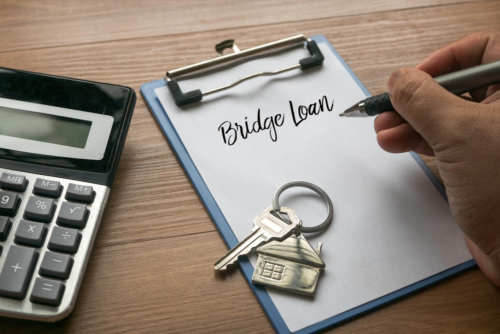 Selective focus of calculator, house key, and hand writing Bridge Loan on a clipboard with white paper.